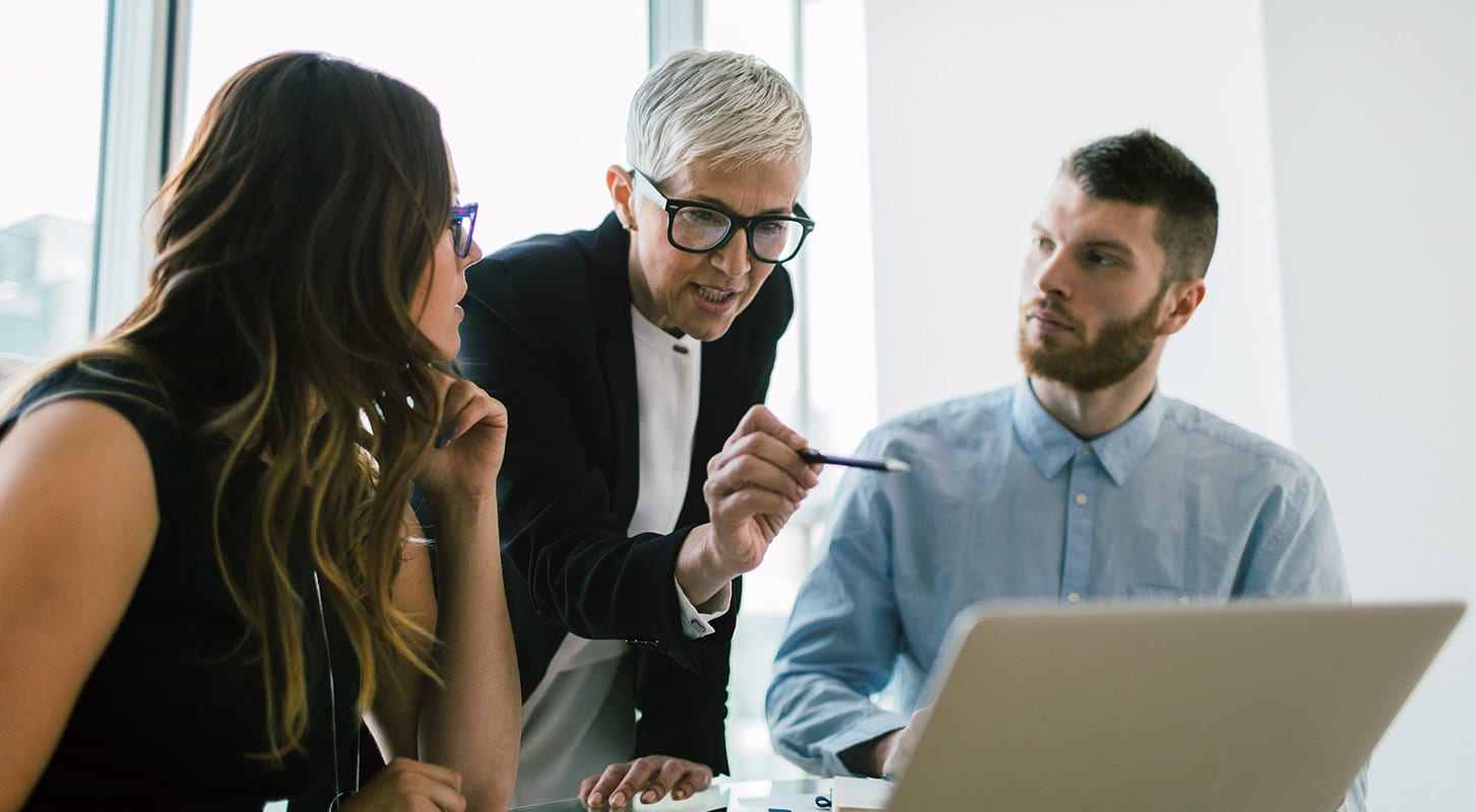 Trois personnes discutent en regardant un ordinateur portable sur la table devant eux.